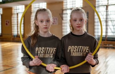 Twin girls in gym holding a hula hoop, wearing 'Positive Thoughts' sweatshirts.